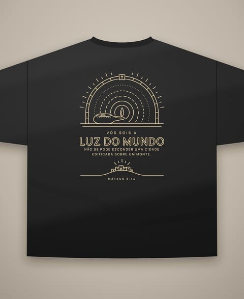 Ilustração em escala da camiseta LUZ DO MUNDO de costas: a candeia acesa num nicho de pedra, os anéis de luz, o versículo e a cidade sobre o monte, em ouro claro.